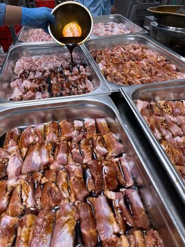 Marinade being poured over sliced pork belly during ingredient preparation in a food manufacturing facility. Marinating process supporting flavor development, product consistency, and commercial meat 