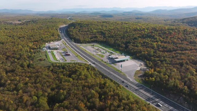 Otocac, Croatia, 22nd October 2025: AERIAL: Motorway rest area and gas station surrounded by colourful autumn forest. Service stops along winding highway while driving through scenic landscape in fall