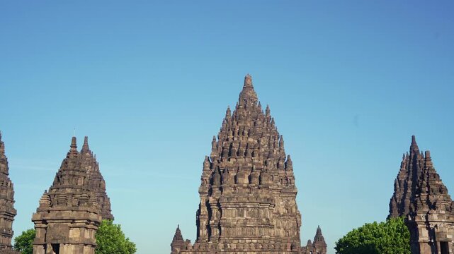 Central Prambanan Temple tower rises between smaller stone spires against a brilliant cloudless tropical sky.