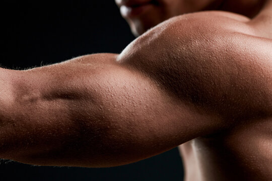 Muscular arm flexes with defined biceps and triceps. Dark background highlights skin texture and muscle tone. No face is visible, focusing on strength and form. Ideal for fitness, bodybuilding