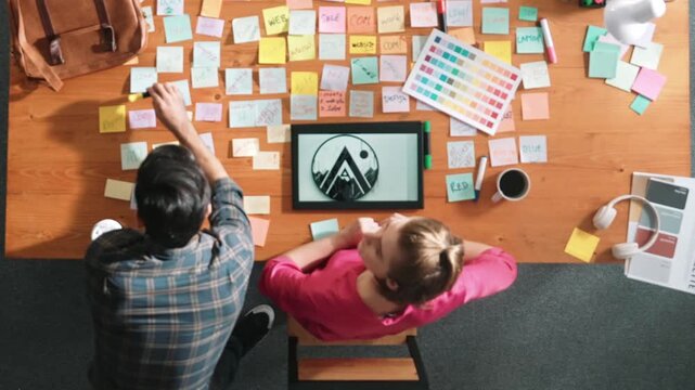 Top view of manager writing idea on sticky notes and explain idea about web design. Professional marketing team or programmer brainstorming idea while looking at tablet with color palette. Symposium.