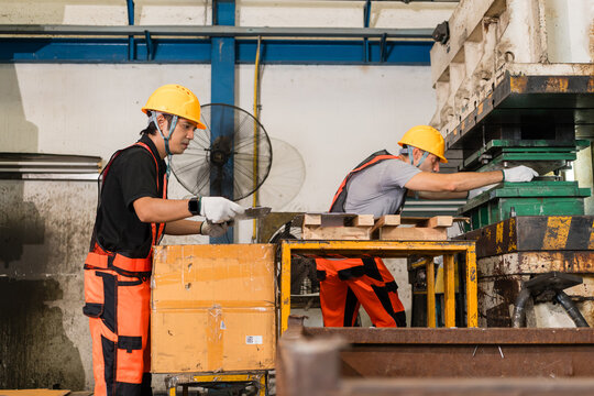Two workers adjusting green die tooling inside open power press machine supporting efficient production and workplace safety inside a busy metalworking factory setting