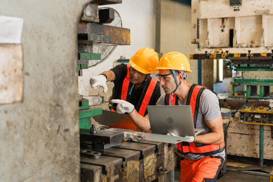 Engineer directing coworker's attention to press die with metal part in hand ensuring precision and quality in a modern industrial manufacturing environment with heavy machinery
