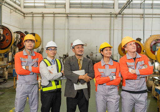 Confident factory team posing near power press machinery in metal stamping plant highlighting skilled labor and industrial teamwork in the automotive parts manufacturing sector