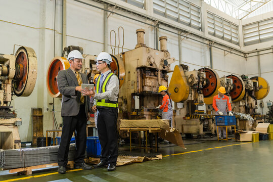 Plant Manager And Engineer Discussing Tablet Report Beside Power Press Machines And Steel Coils ensuring precision and quality in a modern industrial manufacturing environment with heavy