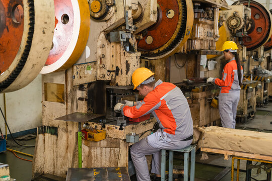 Machine operator adjusting die on power press machine in metal stamping factory ensuring precision and quality in a modern industrial manufacturing environment with heavy machinery