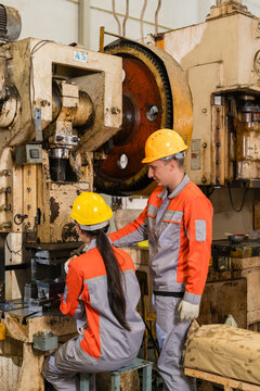 Two Factory Workers Inspecting Mechanical Power Press Flywheel And Gear Assembly In Metal Stamping Shop ensuring precision and quality in a modern industrial manufacturing environment with