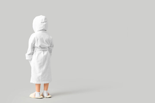 Cute little girl in bathrobe on light background, back view