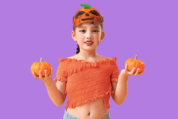 Obraz premium Young girl in pumpkin mask and orange top holding two small pumpkins for halloween celebration, She has playful face paint and a braided hairstyle