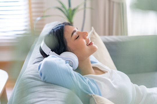 Portrait of Asian woman relaxing listening audio with headphones sitting on a couch at home