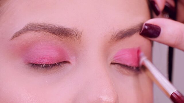 Eyeshadow application. Makeup routine. Artist using professional brush pink color product to woman eyelid treatment.