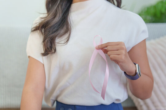 Woman holding pink ribbon on chest for breast cancer awareness campaign