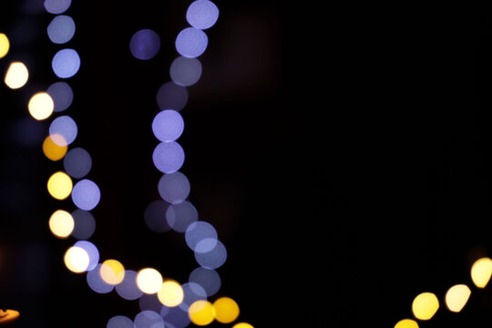 White and lavender bokeh light chain with wide dark copy space on black background