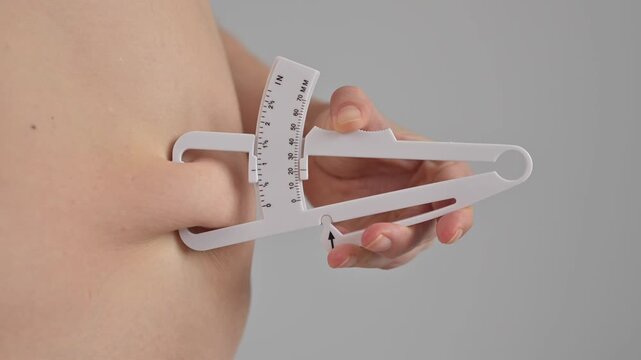A woman measures the amount of subcutaneous fat on her abdomen using a caliper.
