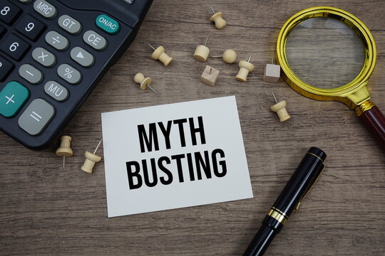 Myth Busting text written on notepad with pen, magnifying glass and calculator on wooden background