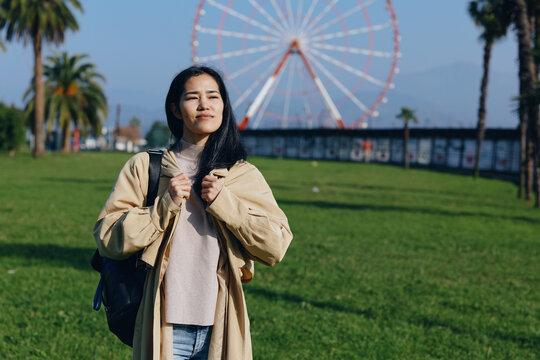 Traveler posing in a park with a distant ferris wheel on a sunny day, casual jacket and backpack, capturing a moment of exploration and relaxed outdoor style.