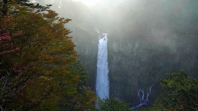 Kegon falls in nikko national park japan during misty autumn morning with dramatic cinematic lighting and vibrant fall foliage surrounding vertical water.