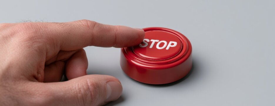 Hand pressing red Stop button on gray background  