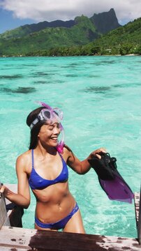 Swimming girl coming out of water after snorkel swim in coral reefs of Tahiti on private overwater bungalow in Moorea, French Polynesia. Luxury travel. Raw vertical video of real woman without makeup