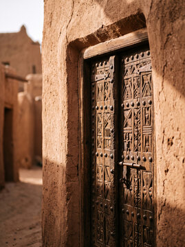 Old rustic carved wooden door in sunlit adobe mud brick wall
