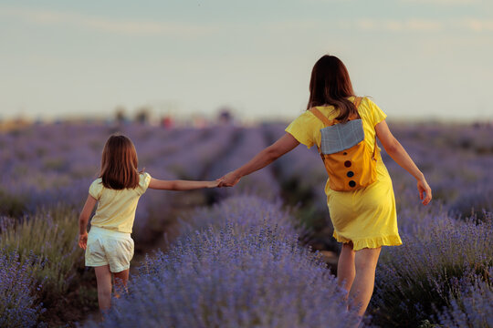 Mother And Daughter Walking With Open Hearts Toward Bright Sunny Horizons. Loving family walks away through purple lavender fields holding hands together