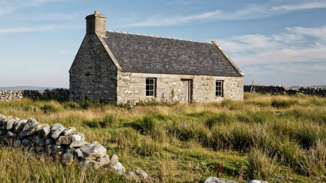 Old stone cottage in a grassy rural landscape with dry stone wall