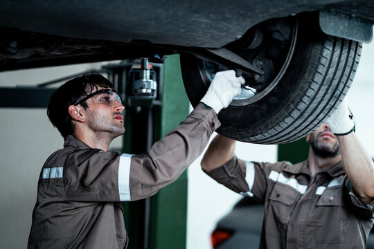 Professional Automotive Technician Carefully Inspecting Vehicle Suspension, Brake Components, and Wheel System Under a Hydraulic Car Lift During Routine Maintenance and Repair Service in a Modern Auto