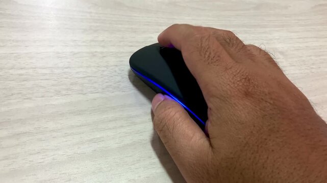 man hand using wireless computer mouse with blue led light on wooden desk