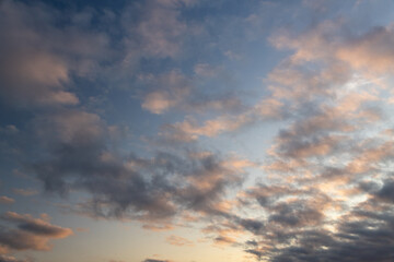 Fototapeta premium Beautiful sunset sky background with soft pink and orange clouds at dawn. Scenic dramatic cloudscape texture in evening twilight. Natural weather concept of blue heavens with bright sunbeams.