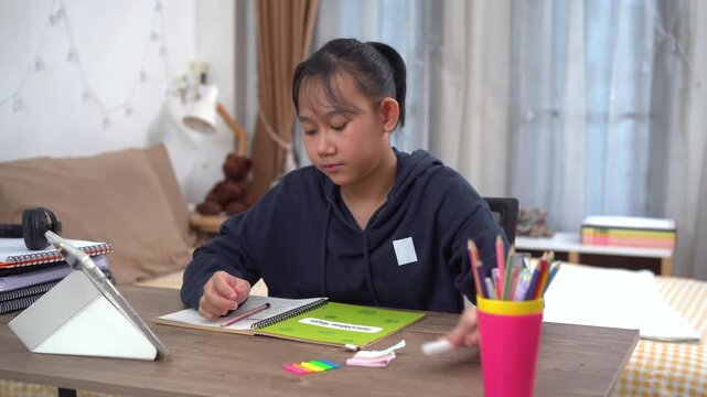 Young girl is diligently taking notes on important points from lesson during an online class at home