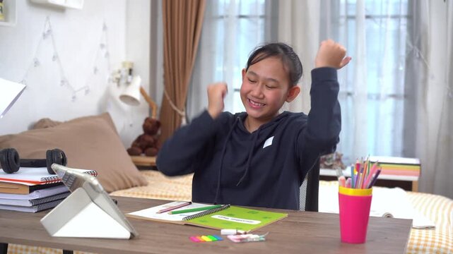 Young girl smiled happily and raised her arms in delight after answering the question correctly during her online lesson