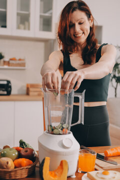 Woman preparing green smoothie in bright kitchen with fresh fruits and vegetables, healthy eating lifestyle moment in natural daylight