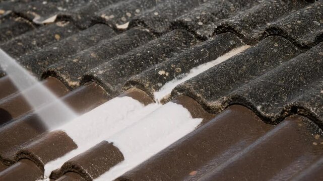 Close up of roof cleaning with high pressure water removing dirt and moss from brown tiles