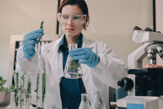 Scientists in lab coats work with plants in a modern lab, focusing on research and experimentation under bright, sterile conditions.