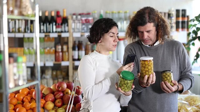 Couple scans barcode QR code on pickled olives label package, follows link and studies information for consumer in supermarket application. Client seek olives manufacturer data in on-line marketplace
