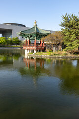 Naklejka premium Traditional Korean pavilion by a lake with water reflection and modern building background vertical composition