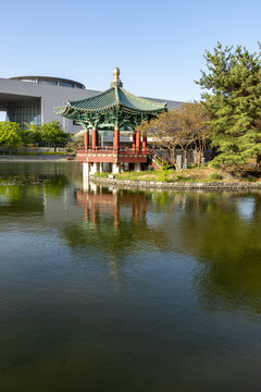 Traditional Korean pavilion by a lake with water reflection and modern building background vertical composition