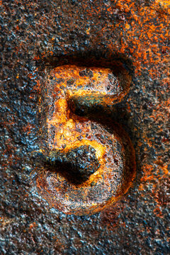 Close up of the number five on an aged cast iron surface covered with natural rust and patina