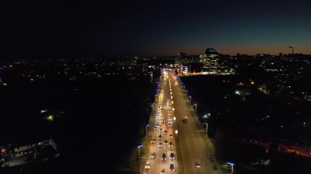 Aerial view of a busy highway bridge at night with heavy traffic and city lights.