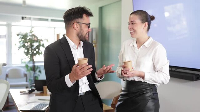 Man and a woman work in an office, they stand near a table and drink hot coffee during a work break