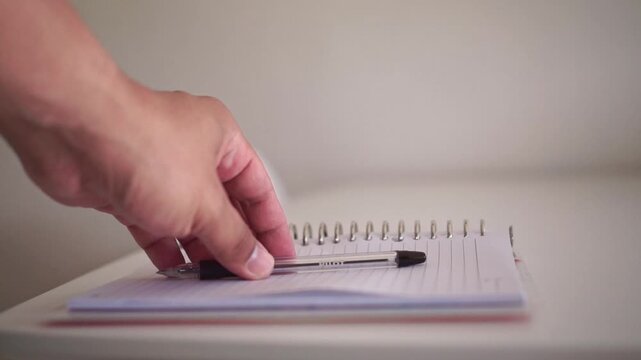 Person gently sets a ballpoint pen on an open notebook, symbolizing task completion, planning, and daily note-taking in a clean workspace.
