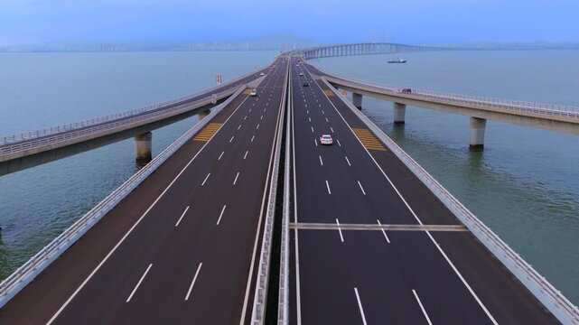 Evening twilight drone shot of Qingdao cross-sea highway, moving traffic and logistics trucks on giant bay bridge, landmark coastal infrastructure of Shandong China