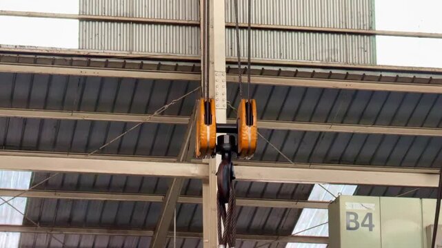 Overhead crane hook and pulley system in industrial warehouse. Manufacturing, heavy industry, and factory equipment concept footage.