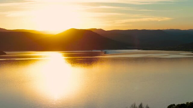 Breathtaking landscape shot filmed through forest trees capturing multiple firefighting Canadair aircraft taking off in formation from a calm lake surface, backlit by a brilliant golden hour sunset.