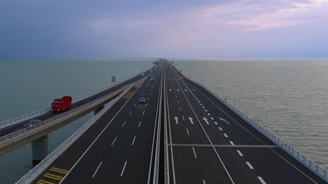 Aerial drone view of Qingdao Bay Cross-sea Bridge during blue hour dusk, heavy cargo trucks and vehicles driving on marine viaduct, grand Chinese transportation infrastructure