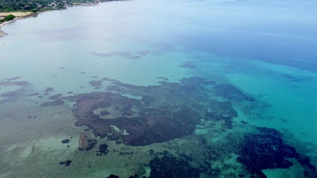 Drone footage of the crystal-clear turquoise waters and rocky reef formations at Kanoni Beach on Lesvos Island, Greece, showcasing the tranquil Aegean coastline on a sunny summer day.