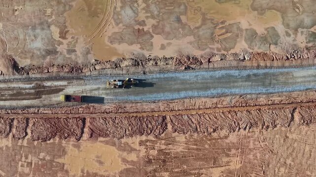 Top down aerial shot of grader and dump truck preparing gravel road through red earth construction zone