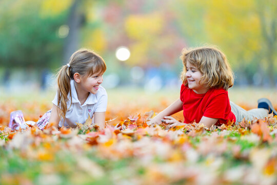 Autumn kids throw leaves. Autumn play on grass. Happy children enjoy autumn park. Fallen leaves mark autumn fun.