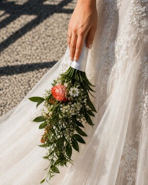 Bride holding cascading floral bouquet beside lace wedding dress