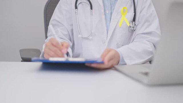 doctor using laptop and report notes on notebook for Gold Yellow Ribbon for concept of September Childhood Awareness month, July Sarcoma, bone and bladder, support survivor. World Cancer day